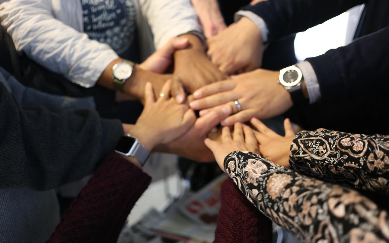 Several multiracial hands are clasped 