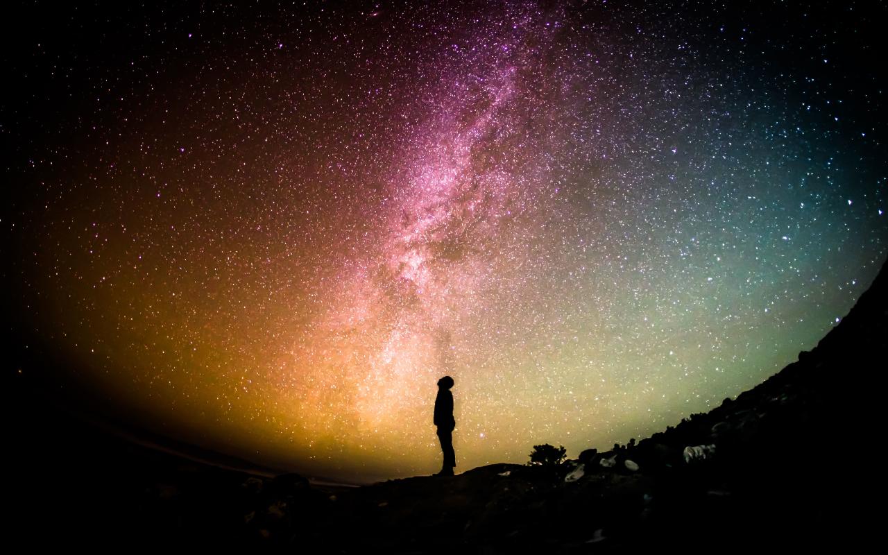 A person stands in a valley at night with a starry sky