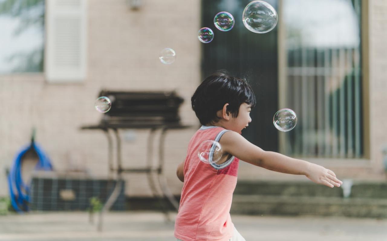 A child blows bubbles outside of a house