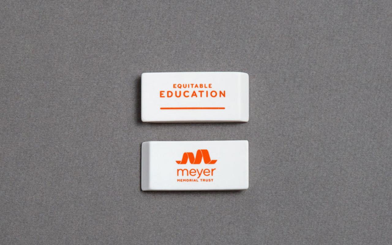 On top of gray cloth sits two erasers that read: Equitable Education...Meyer Memorial Trust