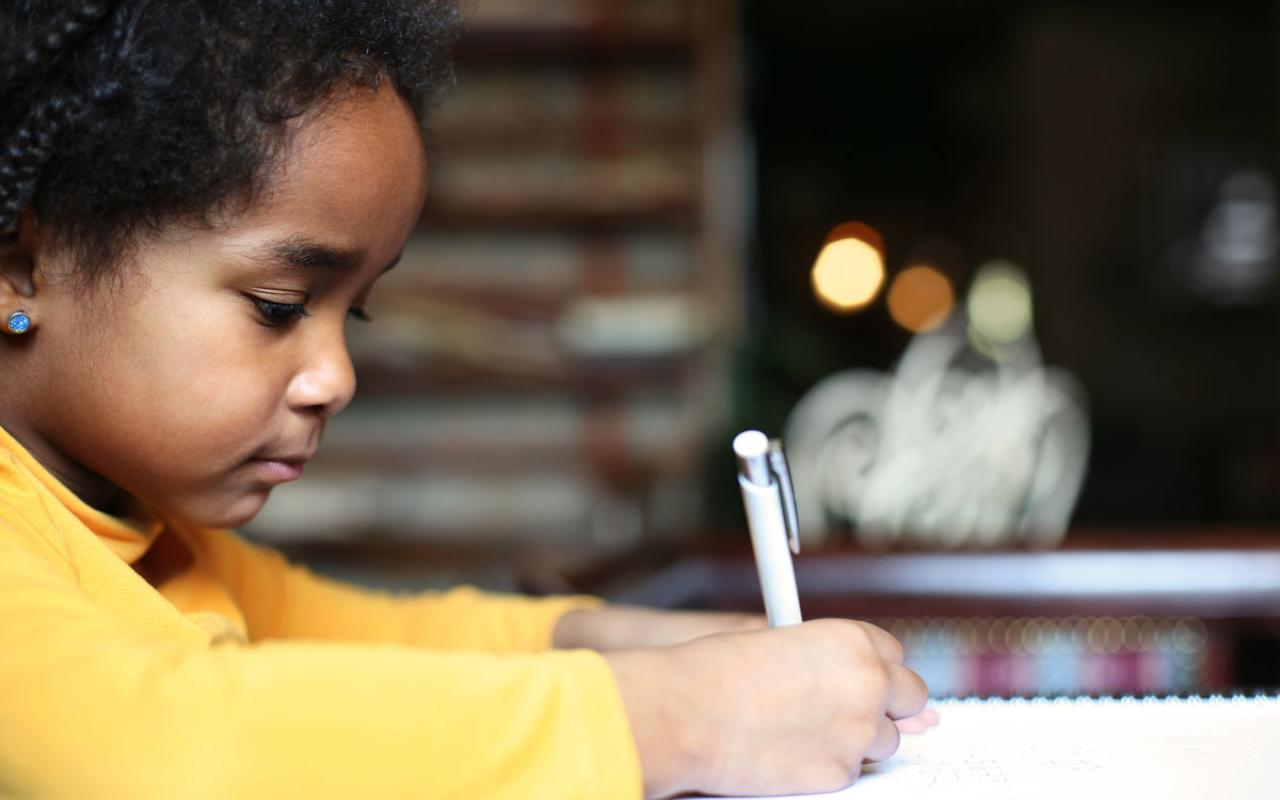 Photo caption: A little girl in a yellow sweater takes notes during class.