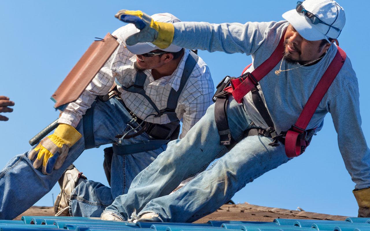 Photo caption: Two contractions applying ceramic roofing atop a roof.