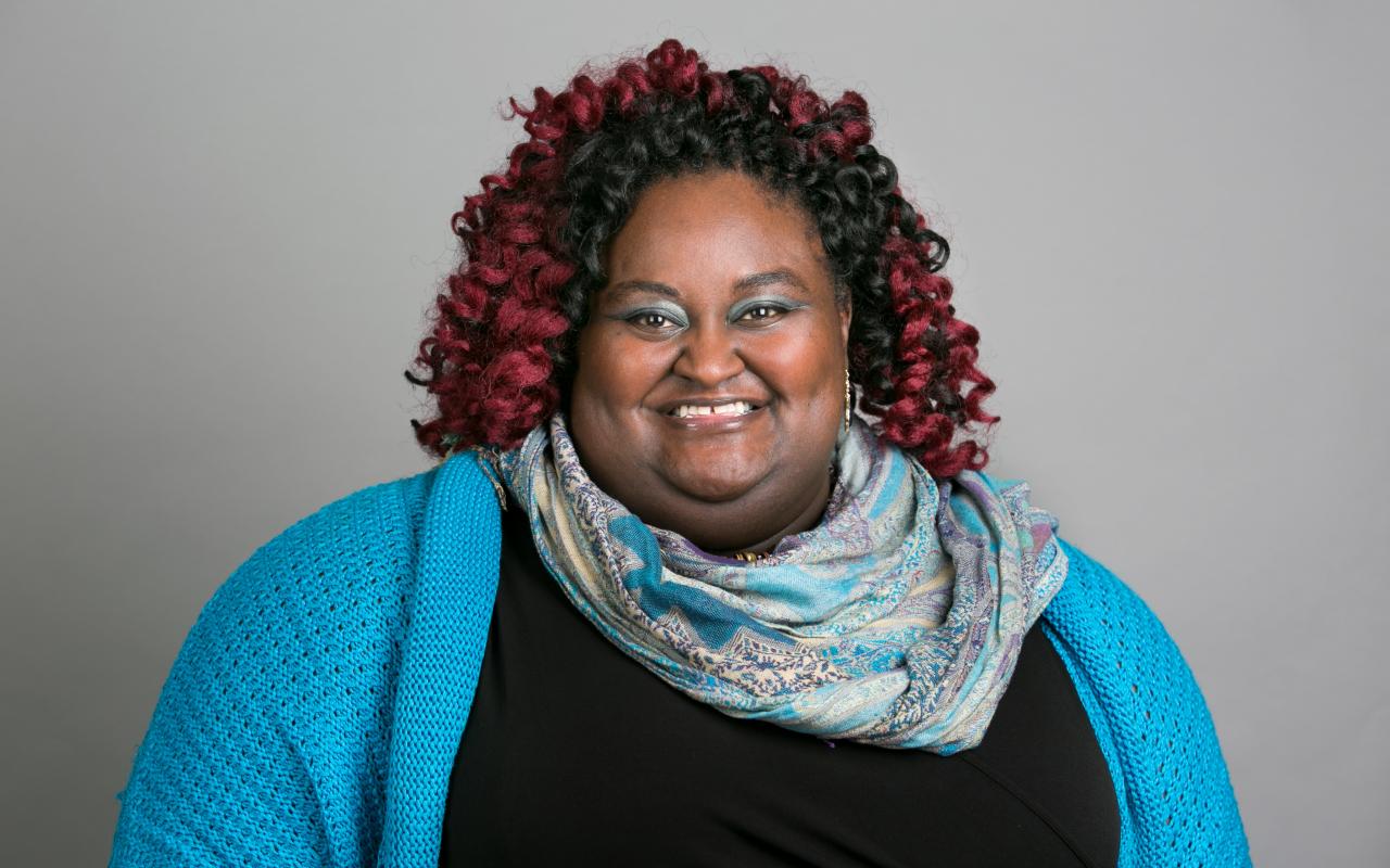 A photograph of Kimberly Melton wearing a bright blue cardigan and scarf.