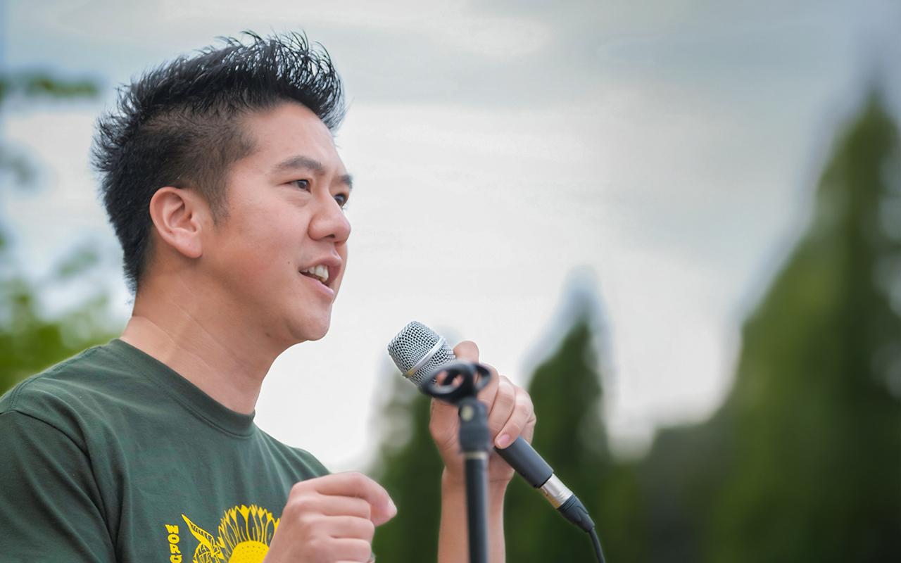 Huy speaking outdoors at a microphone