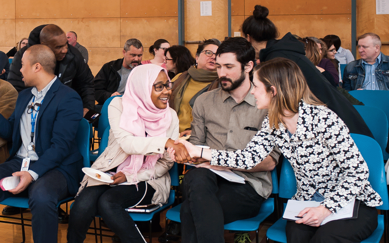 In the gymnasium at Immigrant and Refugee Community Organization (IRCO), two grantseekers greet and shake hands during a 2018 funding information session for Meyer’s Annual Funding Opportunity.