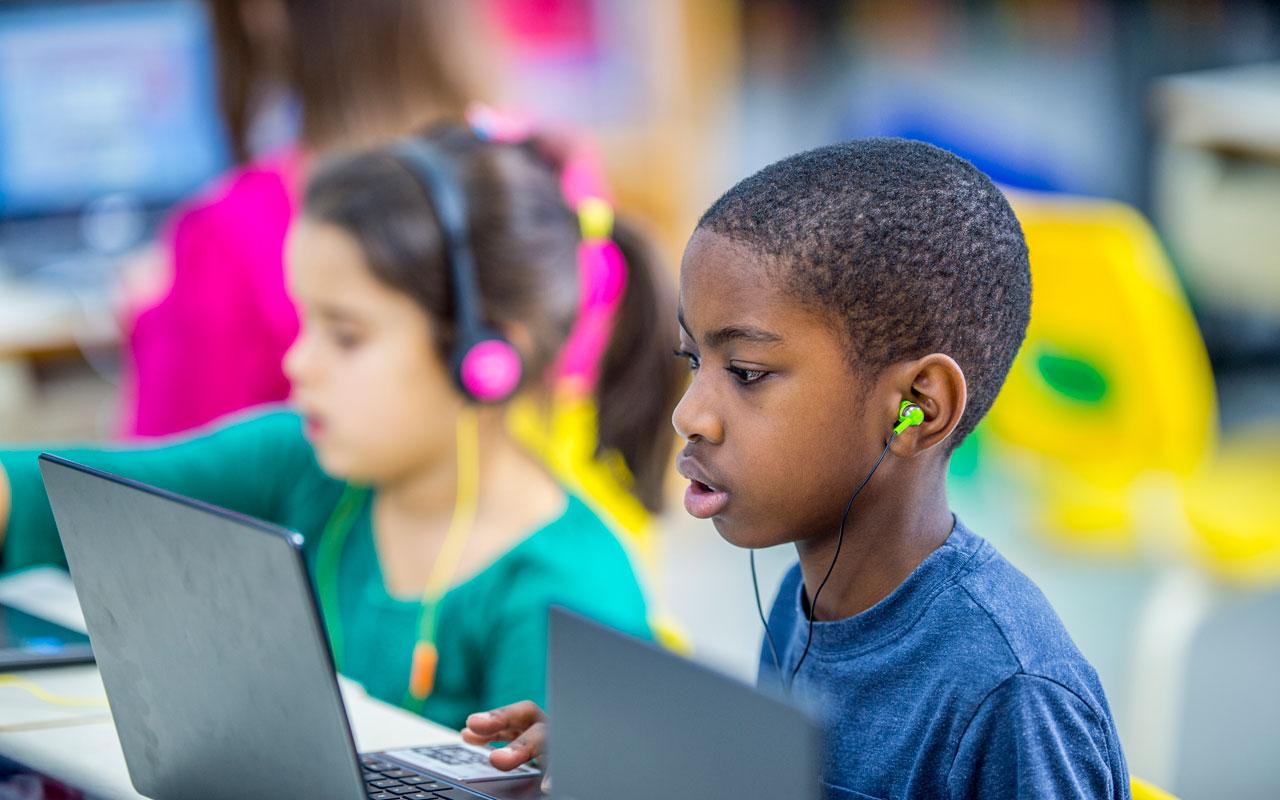 Photo caption: Foreground, a young child listens to a book on a computer.
