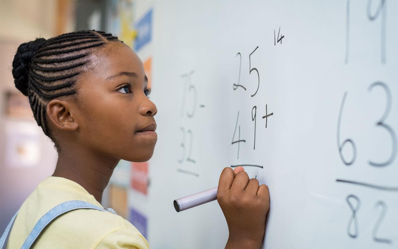Photo caption: a young woman with cornrows completes a math equation.