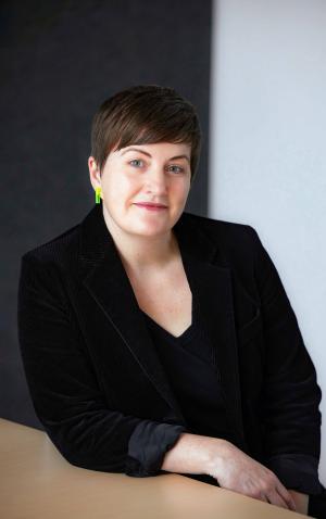 A portrait of Erin in a black blazer sitting at a table